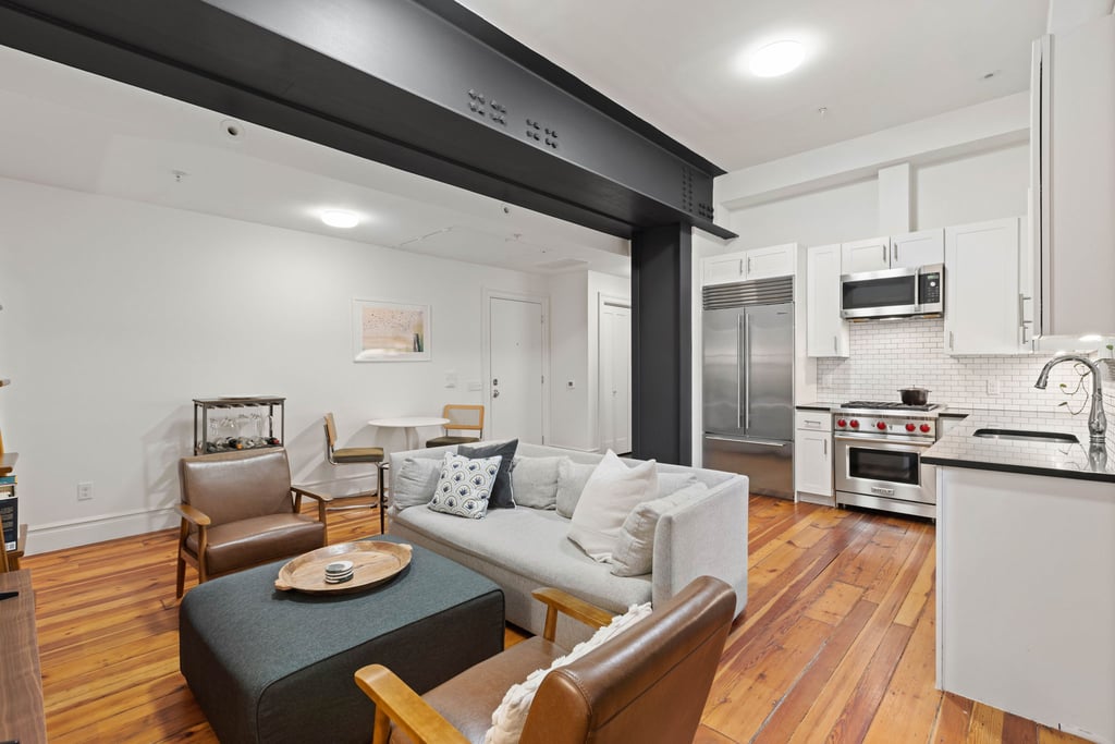 Living room with exposed steel beam, wood floors and open kitchen at 260 First Street unit 1A in Jersey City